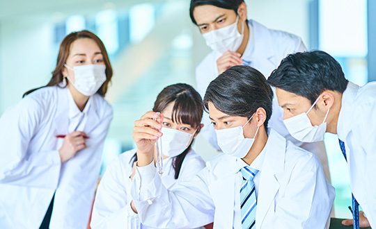 Researchers in white lab coats discussing an experiment around a laboratory table.